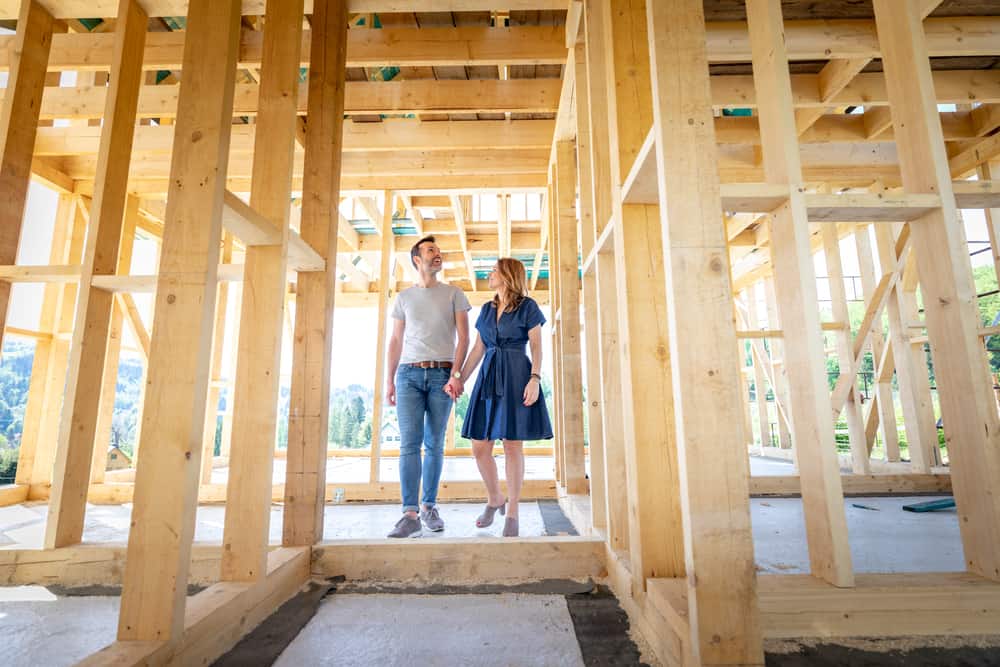 Couple Standing In Structure Of Building Their Own Home.